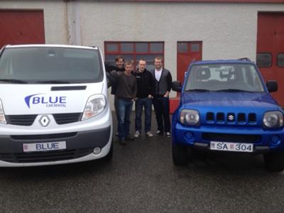 Blue Car Rental staff with airport shuttle and Jimny.